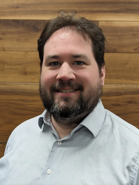 Christian Sabourin, smiling, in front of a wooden wall.